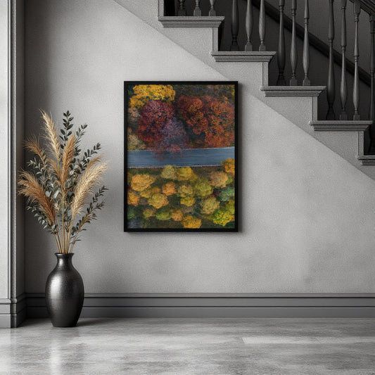 A framed abstract landscape painting featuring vibrant autumn foliage in yellow, orange, red, and green tones, hanging on a gray wall in a modern interior setting next to a black vase with dried grasses and below a staircase.