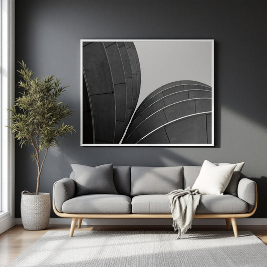 A large black and white framed wall art print depicting curved architectural lines, displayed above a modern gray sofa in a styled living room setting.