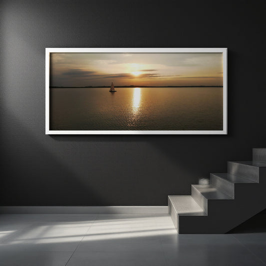 A framed horizontal landscape print of a sunset over water with a small sailboat, displayed on a dark gray wall above a staircase.