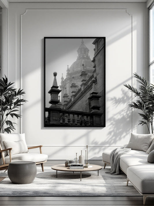 A black and white framed art print of a grand domed building, displayed on a white wall in a modern, sunlit living room with a sofa, armchair, and coffee table.