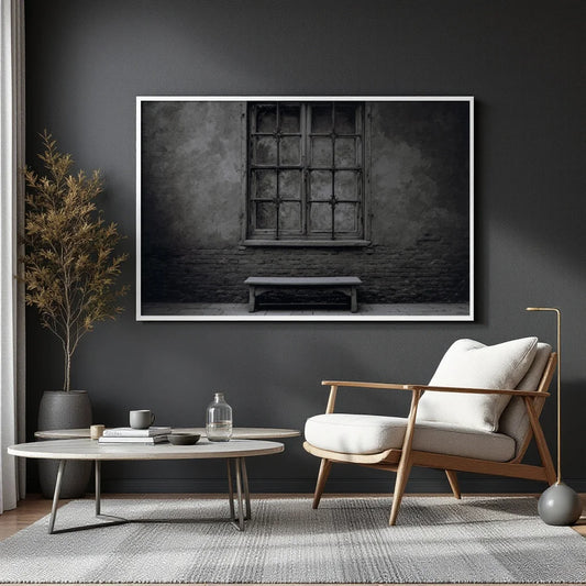 A black and white fine art photograph of an old stone wall with a large multi-paned window and a simple wooden bench below it, presented with a white border.