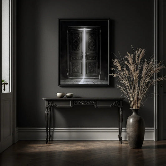 A framed black-and-white art print depicting an open door with light streaming in, displayed on a dark gray wall above a console table in a moody, dimly lit room with a large vase of dried grass nearby.