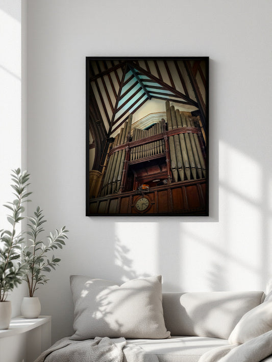A framed vertical art print of a large wooden pipe organ inside a church, displayed on a white wall above a sofa in a modern, sunlit living room.