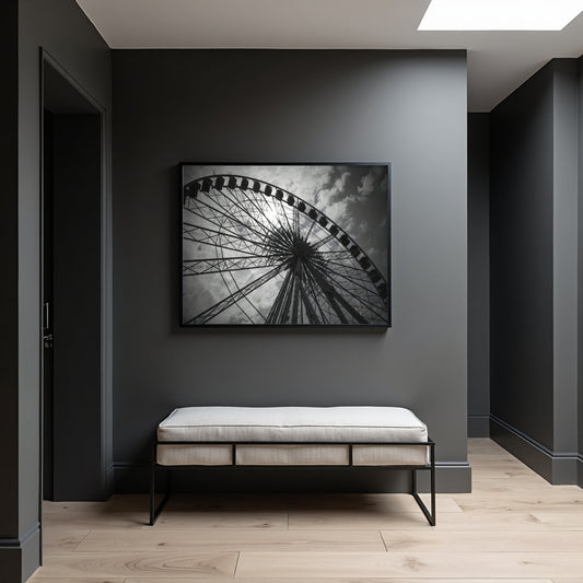 A black and white framed wall art print of a ferris wheel hangs on a dark gray wall above a light beige upholstered bench in a modern entryway with light wood flooring.