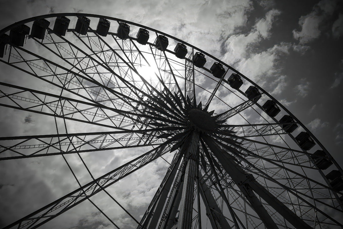 Black and white low-angle photograph of a large Ferris wheel against a cloudy sky.