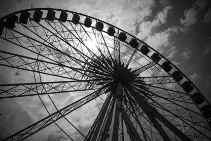 Black and white low-angle photograph of a large Ferris wheel against a cloudy sky.