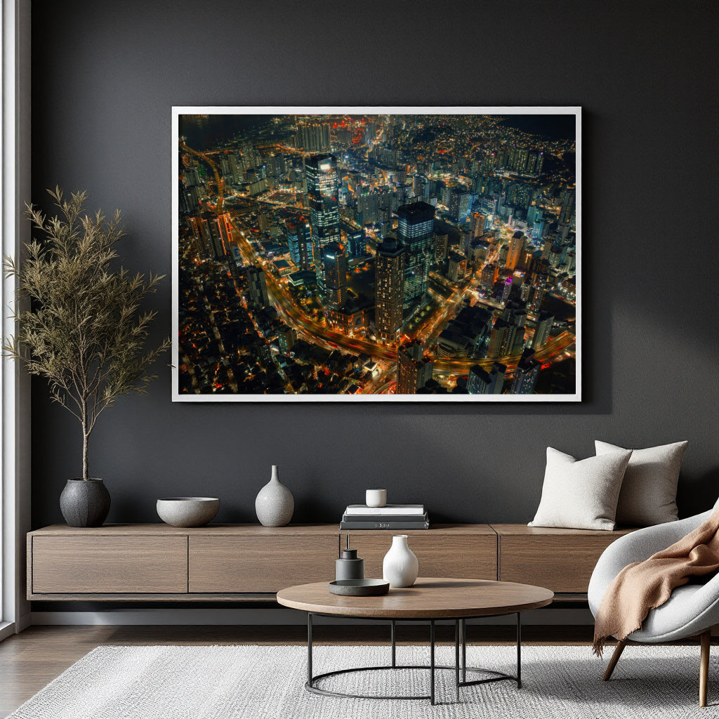 A large framed art print of a vibrant city skyline at night with glowing lights, displayed on a dark gray wall in a modern living room setting above a wooden console table.