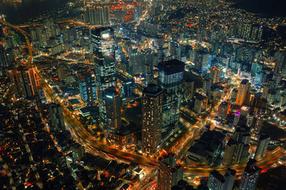 Horizontal Aerial night photograph of a dense modern city skyline with illuminated skyscrapers and glowing street lights.