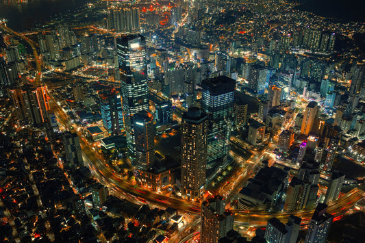 Horizontal Aerial night photograph of a dense modern city skyline with illuminated skyscrapers and glowing street lights.