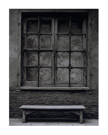 Black and white photograph of an old wooden window with iron bars set in a brick wall, with a simple wooden bench below it.