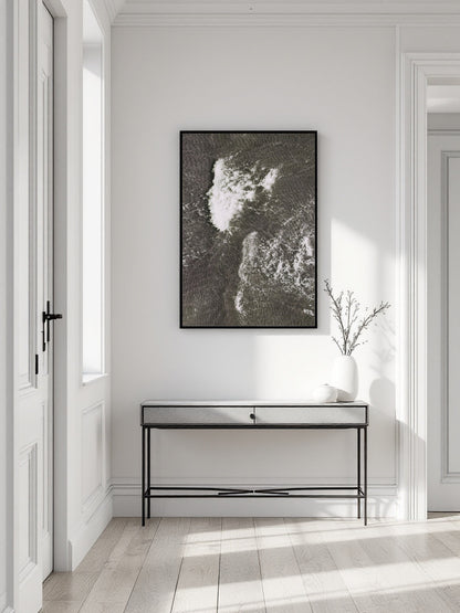 A framed black and white abstract landscape art print hangs on a white wall above a modern console table in a bright, minimalist hallway.