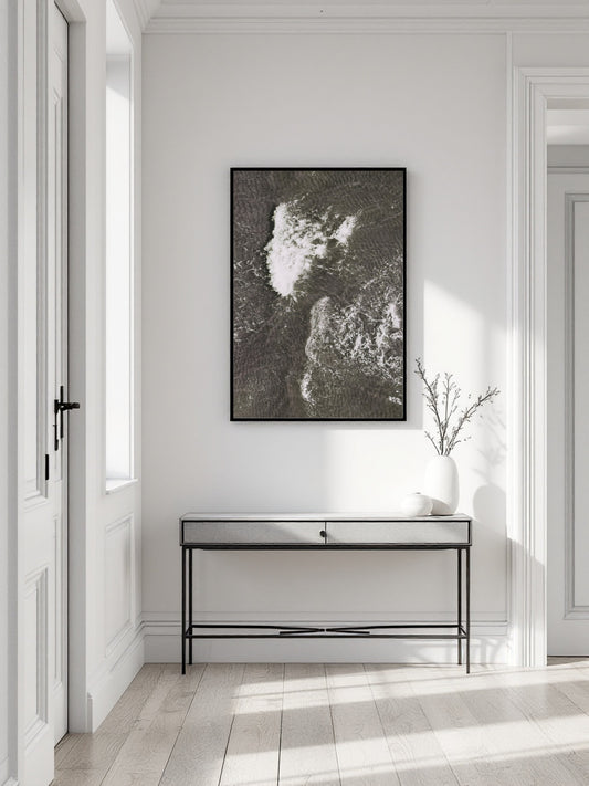 A framed black and white abstract landscape art print hangs on a white wall above a modern console table in a bright, minimalist hallway.