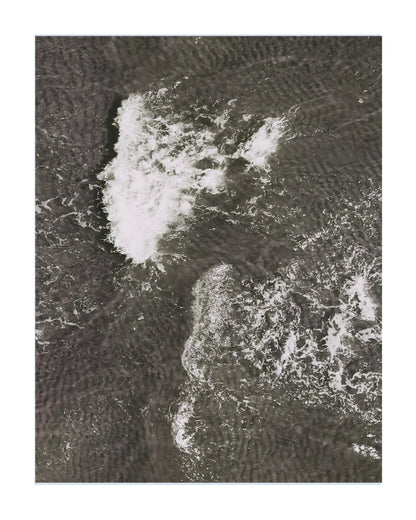 An aerial photograph of dark, textured water with white surf and foam, presented as a square art print with a white border.
