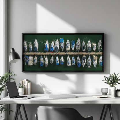 A framed horizontal canvas print of vintage sailboats on a green background, displayed on a light gray wall above a white desk in a modern home office setting.