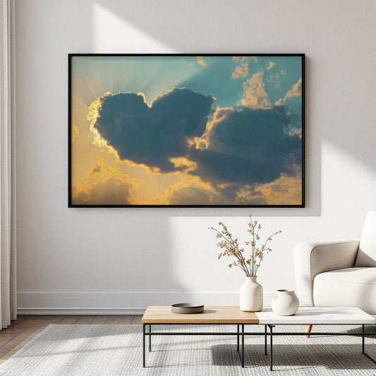 A framed wall art print showing dramatic clouds with warm golden light and blue sky, displayed in a modern living room setting above a low coffee table and white sofa.