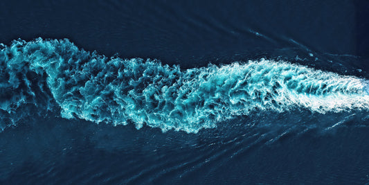 Aerial view of a turquoise and white boat wake cutting through deep blue water.