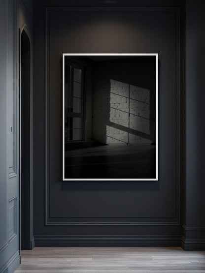 A framed black and white art print depicting a shadow pattern on a wall, displayed on a dark charcoal paneled wall above a light wood floor.