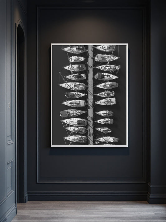 A framed black and white art print depicting a vertical arrangement of small boats on a dark wall in a hallway setting.
