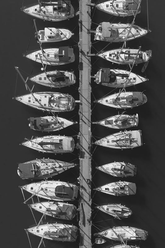 Black and white aerial photograph of multiple sailboats docked side-by-side along a central pier.