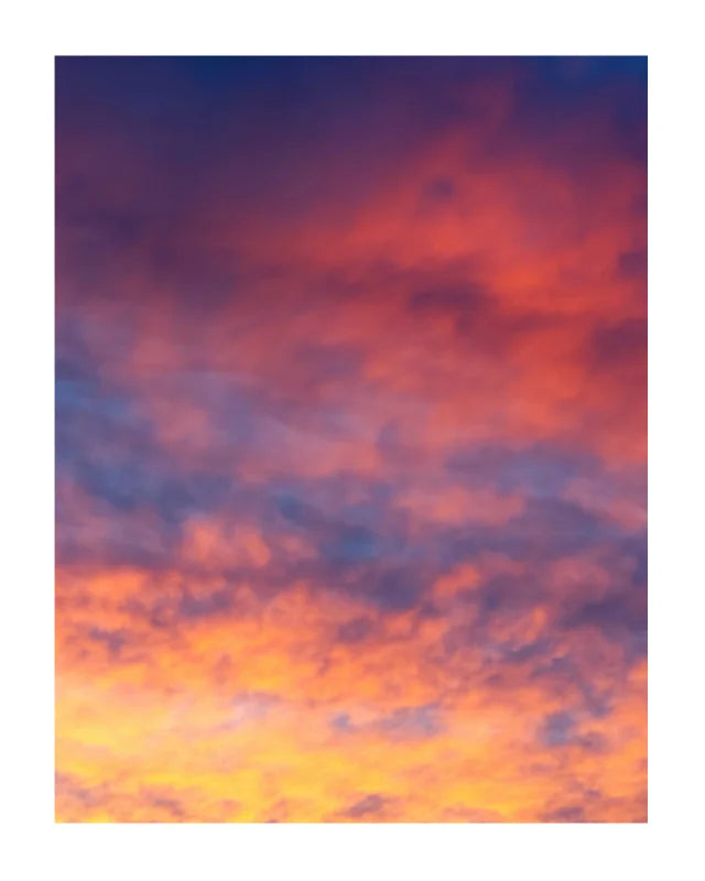 A vertical rectangular print showing a colorful sky with clouds in shades of orange, pink, purple, and blue, centered on a white background.