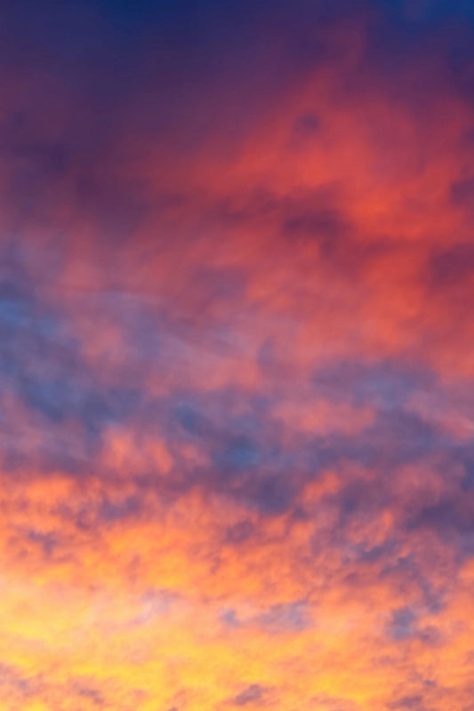 A full-frame view of a colorful sunset sky with clouds illuminated in orange, yellow, purple, and blue tones.