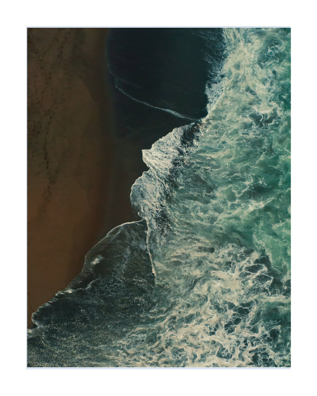 An aerial photograph of a coastline showing dark teal ocean waves with white foam crashing against a brown sandy beach, presented as a square art print with a white border.