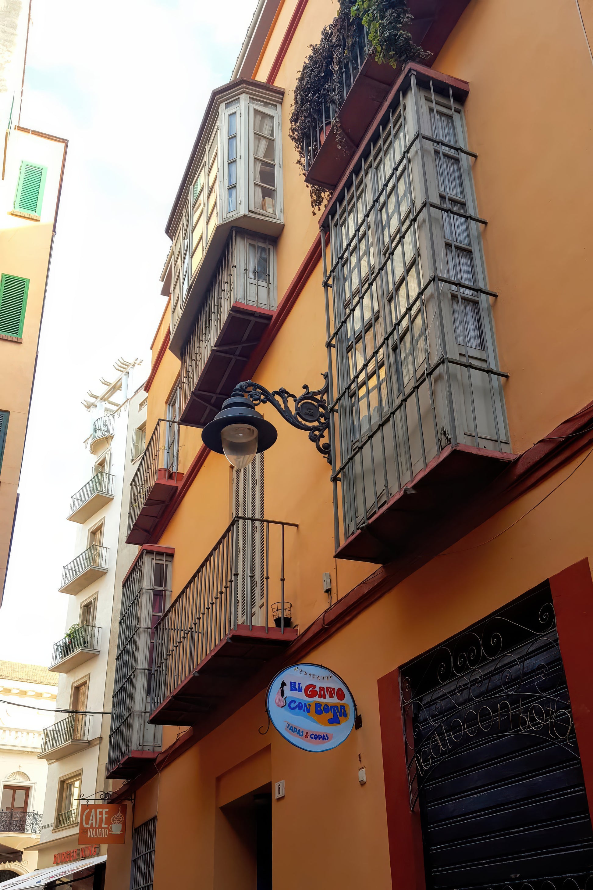 An orange stucco building facade with multiple balconies, metal shutters, a hanging black street lamp, and a round blue-and-white sign reading "I'm Going to Spain.".