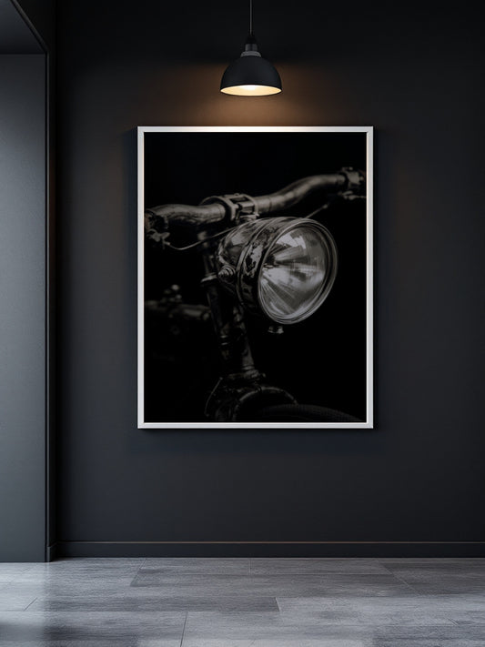 A framed black and white art print of a vintage bicycle headlight hanging on a dark charcoal wall under a hanging lamp.