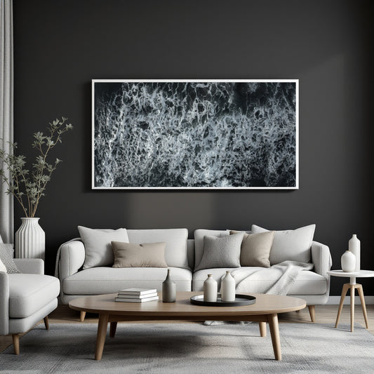 A large framed black and white abstract wave or foam print hangs on a dark charcoal wall above a light gray sofa in a modern living room setting.