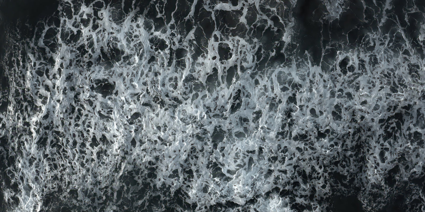 A close-up aerial view of dark water filled with dense white sea foam and churned waves.