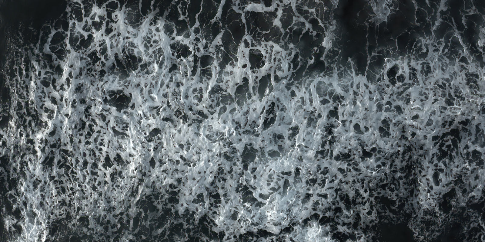 A close-up aerial view of dark water filled with dense white sea foam and churned waves.