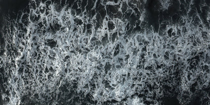 A close-up aerial view of dark water filled with dense white sea foam and churned waves.