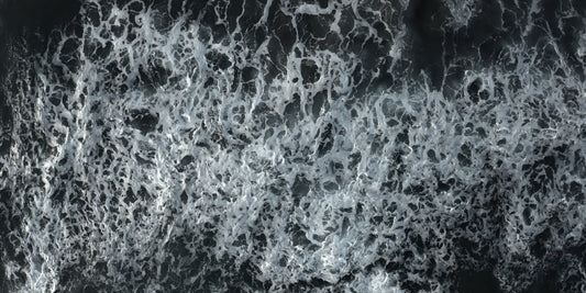 A close-up aerial view of dark water filled with dense white sea foam and churned waves.