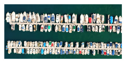 Aerial view of a marina filled with many small boats docked side by side in rows over deep teal water.