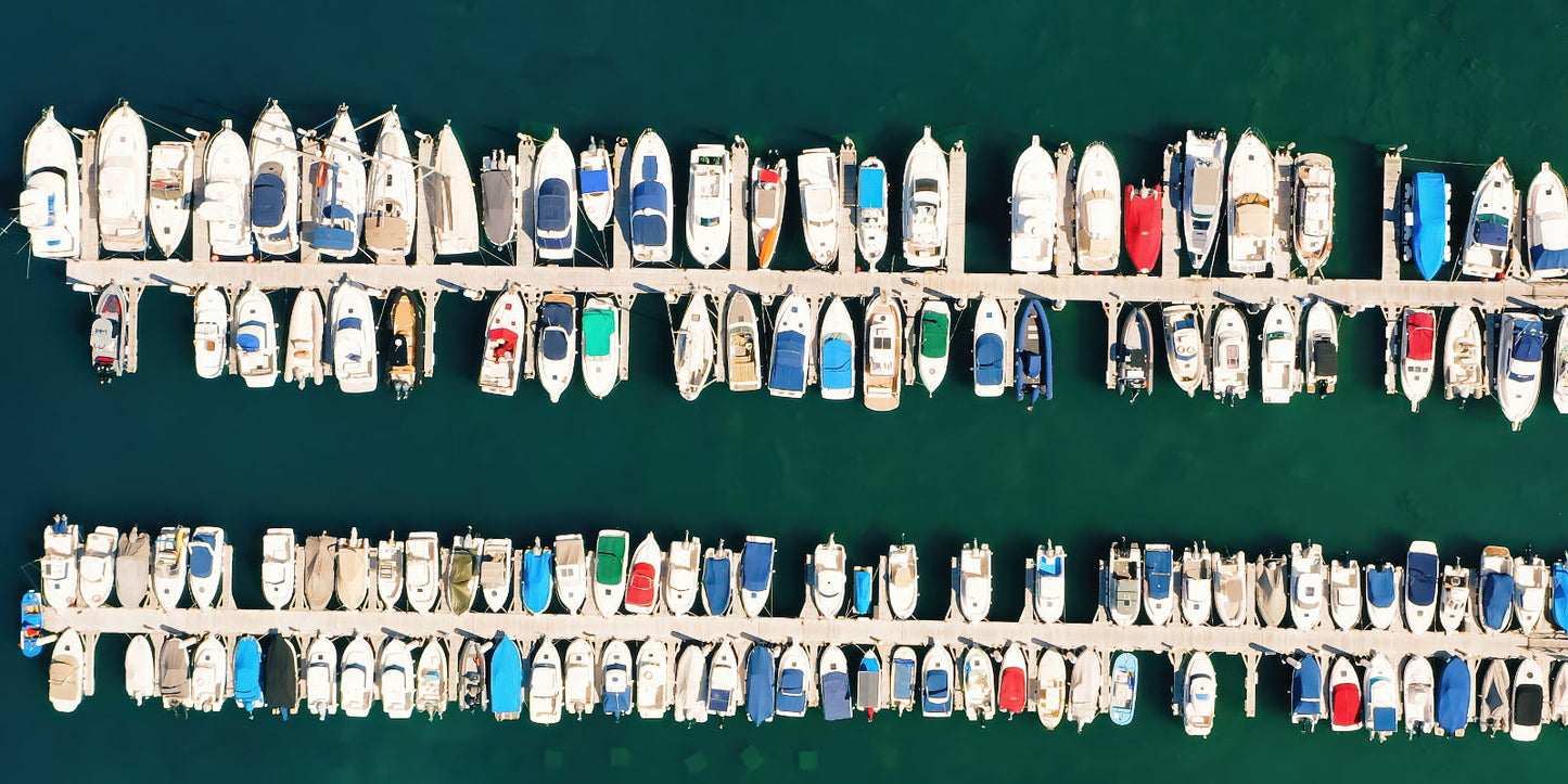 Aerial view of a marina filled with many small boats tied along parallel docks in deep blue-green water.