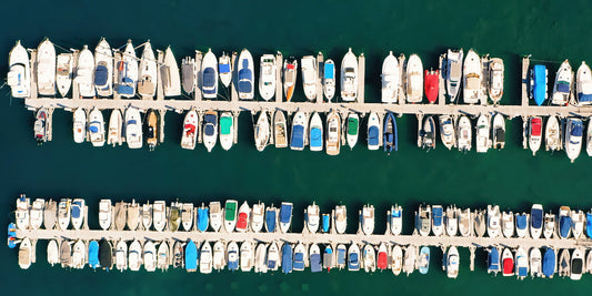 Aerial view of a marina filled with many small boats tied along parallel docks in deep blue-green water.