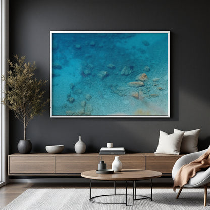 A large framed art print depicting a vibrant blue underwater ocean scene with marine life, displayed on a dark charcoal wall above a modern wooden console table in a styled living room.