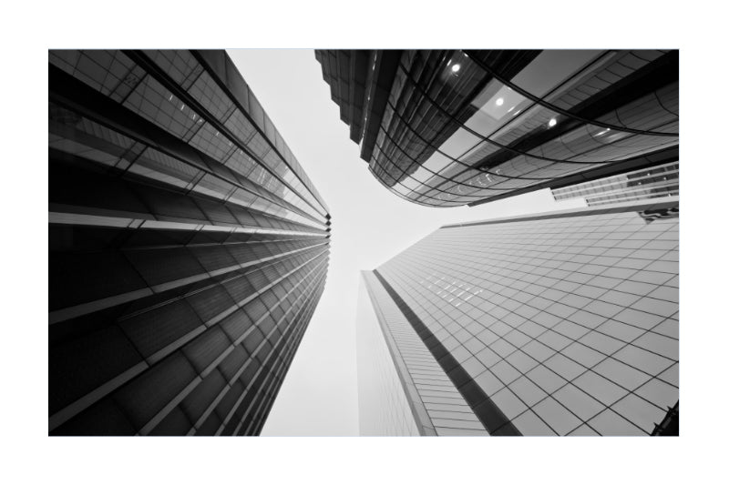 Black and white architectural photograph of modern skyscrapers viewed from a low angle, looking up at the buildings that converge toward the sky.