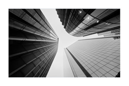 Black and white architectural photograph of modern skyscrapers viewed from a low angle, looking up at the buildings that converge toward the sky.