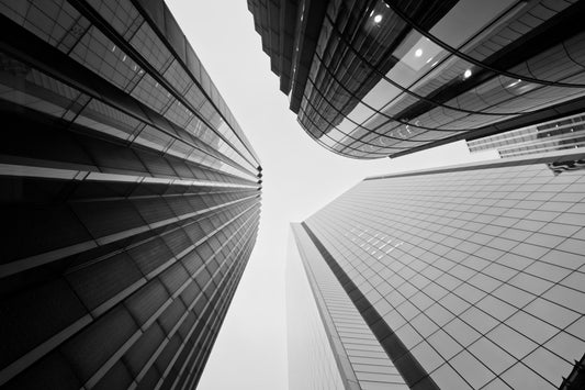 Black and white architectural photograph of modern skyscrapers viewed from a low angle, looking up at the buildings that converge toward the center sky.