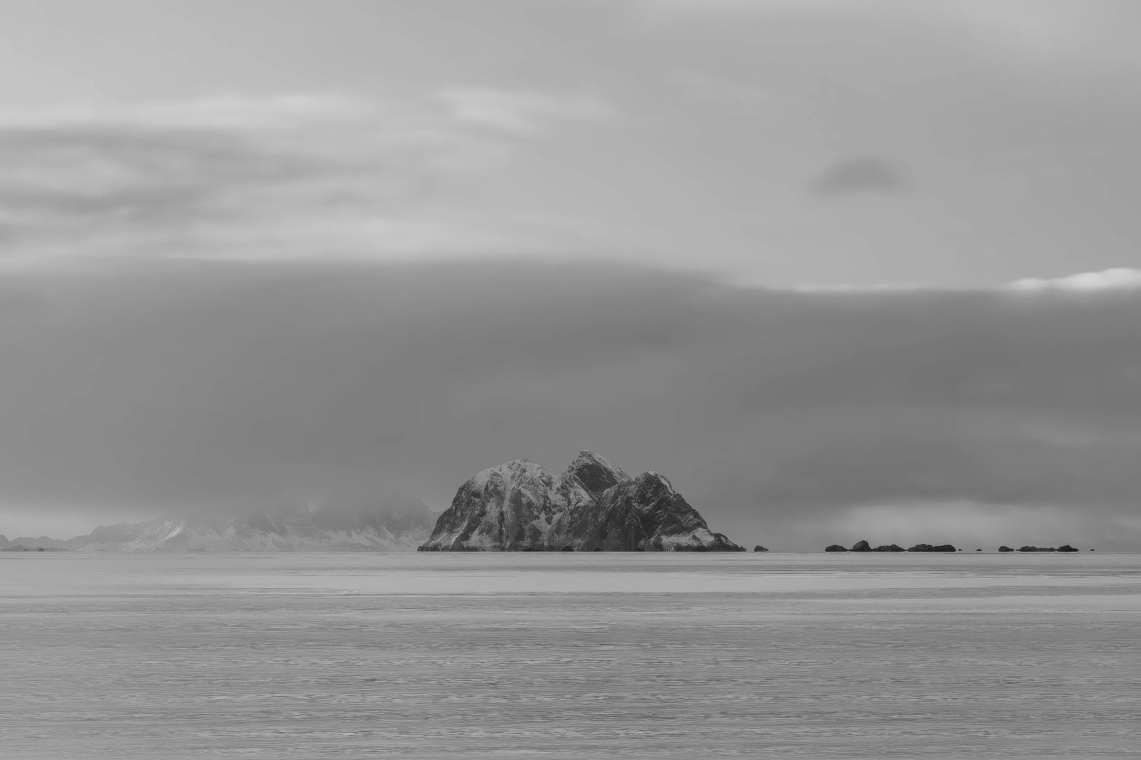 Black and white landscape photograph of a small rocky island rising from calm water under a cloudy sky.