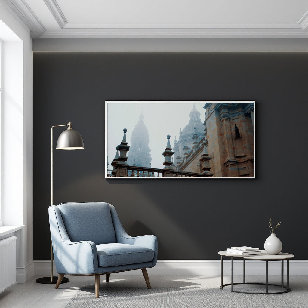 A framed panoramic art print of historic European architecture with domes and towers, displayed on a dark charcoal wall in a modern living room setting with a blue armchair, floor lamp, and side table.