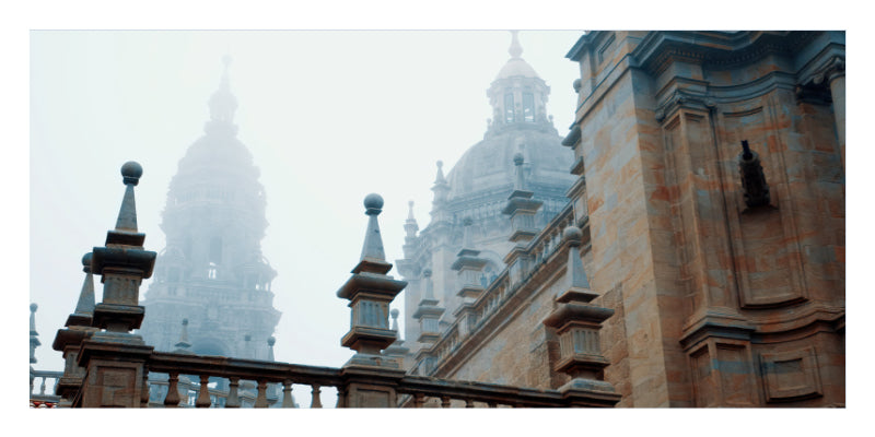 A scenic photograph of a historic stone building with domed towers shrouded in mist, framed by a stone balustrade in the foreground.