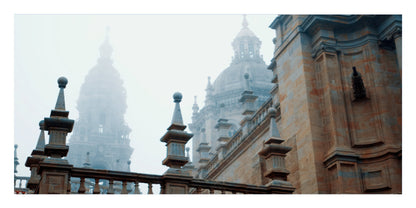 A scenic photograph of a historic stone building with domed towers shrouded in mist, framed by a stone balustrade in the foreground.