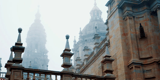 Foggy architectural scene featuring historic cathedral domes and ornate stone spires in soft gray mist, with a warm brown stone building in the foreground.