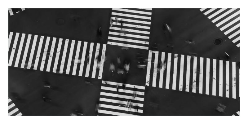 Black and white aerial photograph of a city intersection with crosswalks and blurred figures crossing the streets.