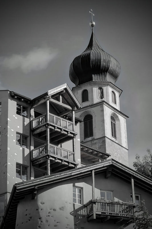 Black and white architectural photograph of a church tower with onion domes, balconies, and surrounding buildings against a cloudy sky.
