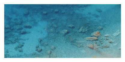 Underwater ocean scene with clear turquoise-blue water, shallow sandy seabed, and scattered rocks.