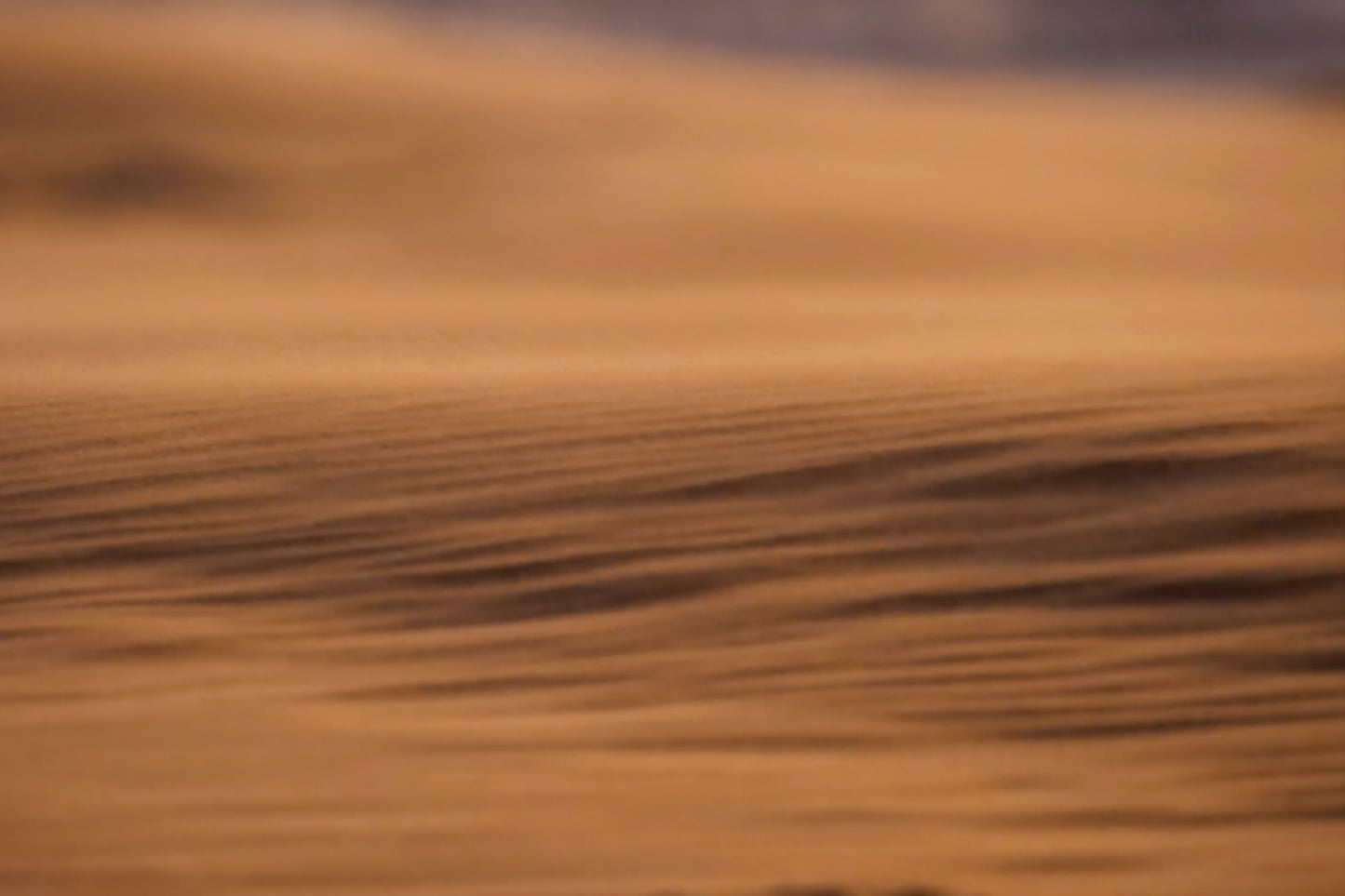 A close-up, abstract view of a warm brown textured surface with soft horizontal ripples and a blurred orange-brown background.