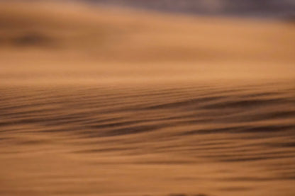A close-up, abstract view of a warm brown textured surface with soft horizontal ripples and a blurred orange-brown background.